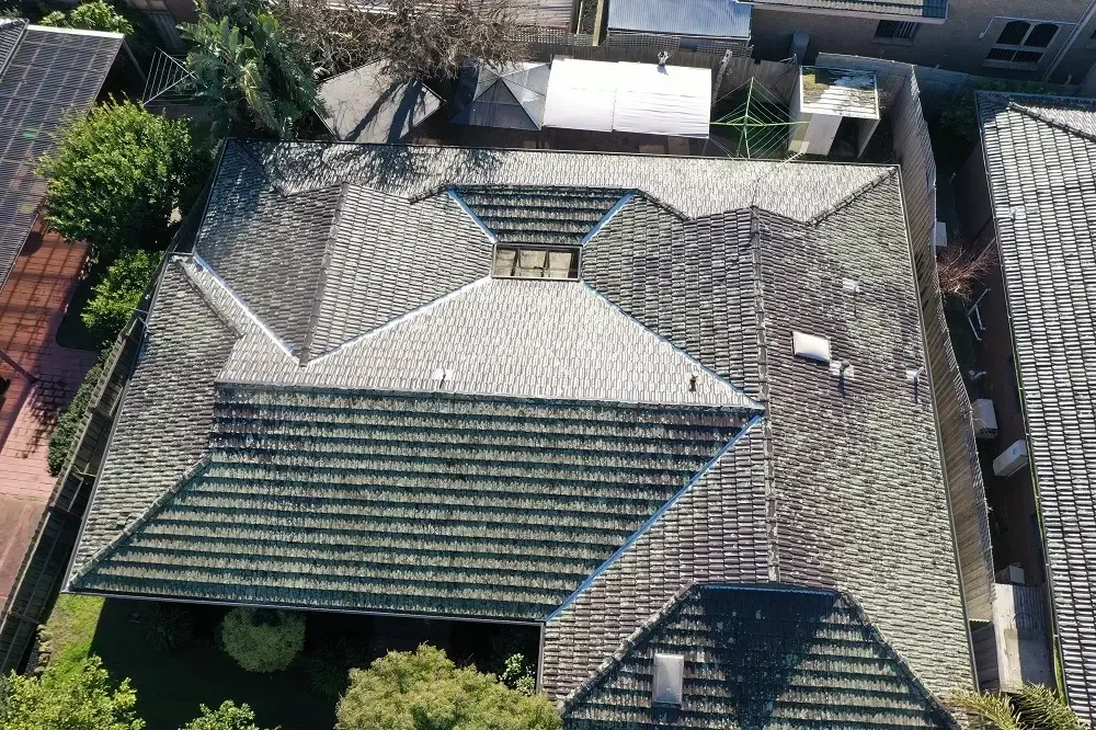 Before: top-down drone view of a weathered, lichen-covered concrete tiled roof