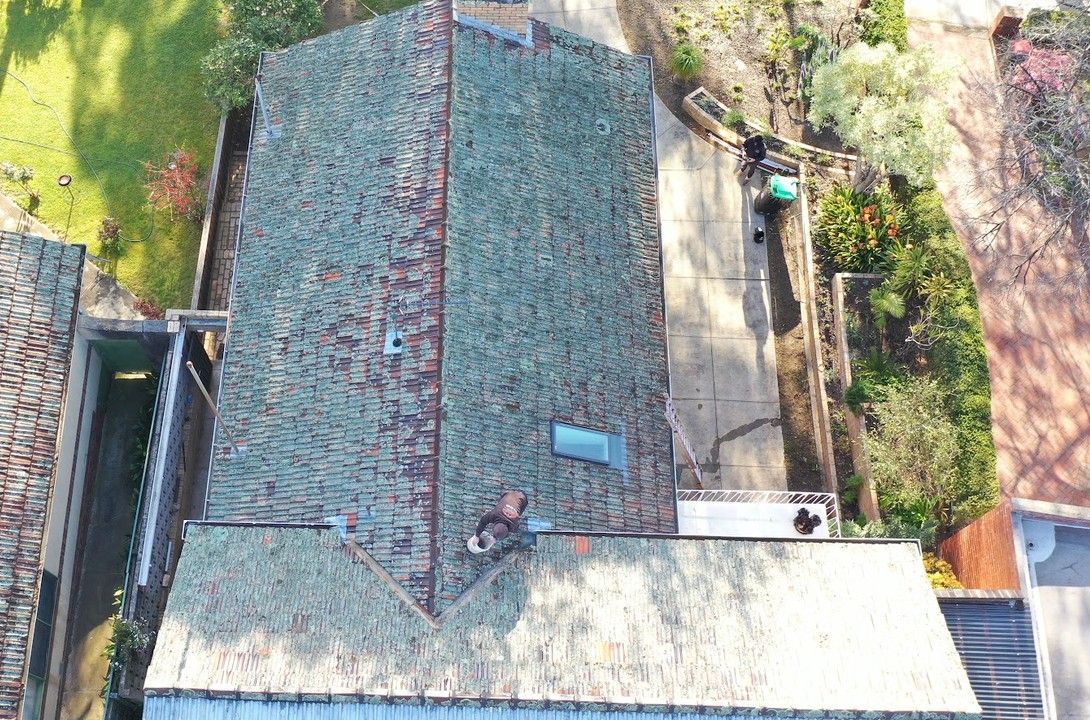 Before: a terracotta tiled roof covered in lichen and moss, seen from above by drone