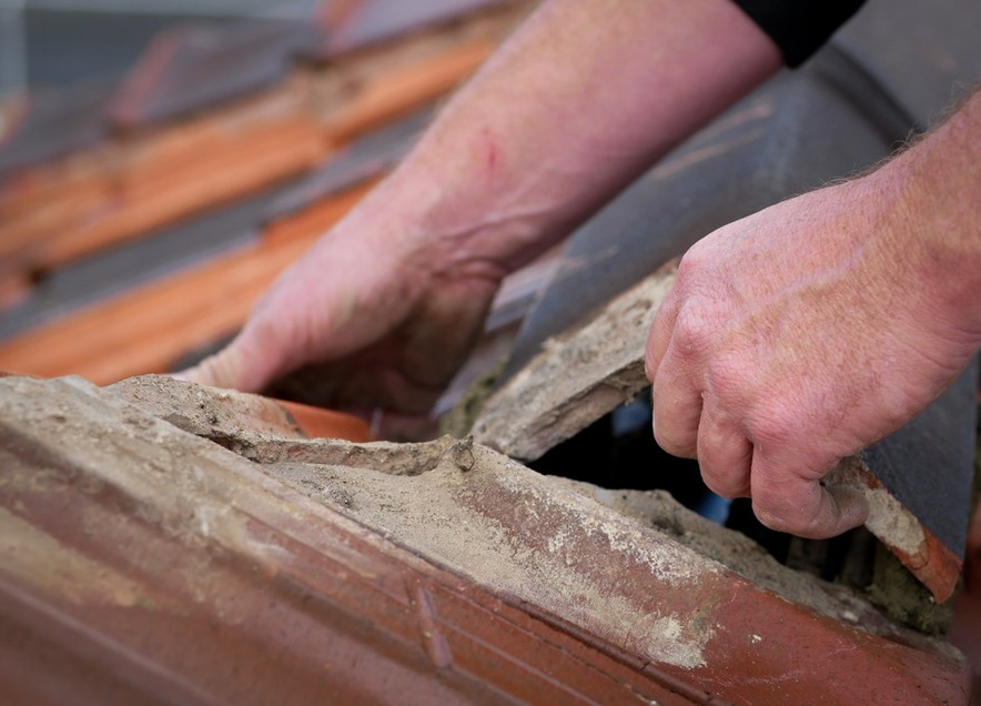 Old, crumbling bedding exposed under a lifted ridge cap — a common hidden cause of roof leaks