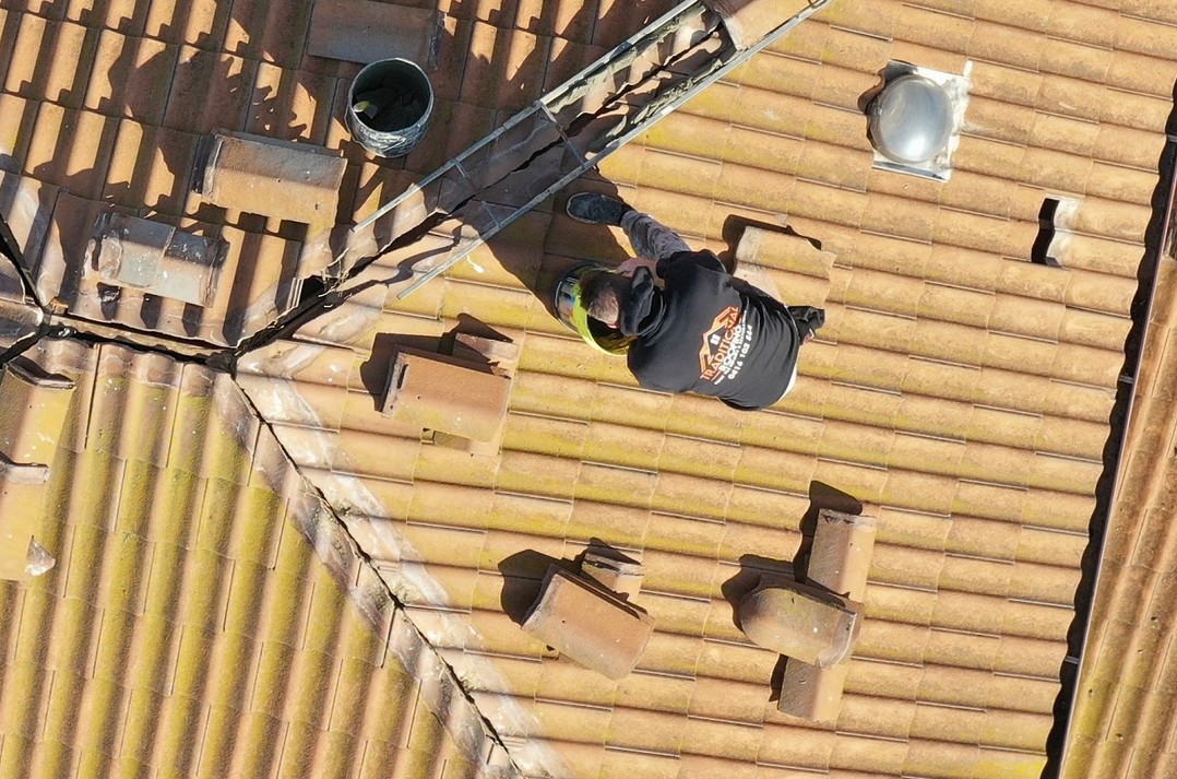 Drone view of a Traditional Roofing roofer working along a weathered terracotta tiled roof with the ridge caps lifted