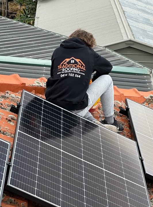 Traditional Roofing team member on a terracotta tiled roof beside solar panels