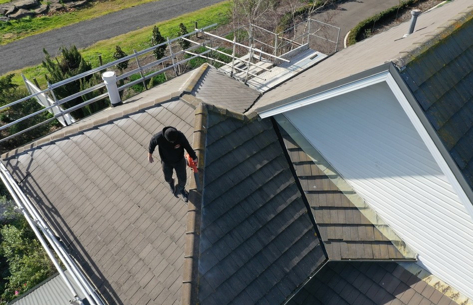 Drone view of a Traditional Roofing roofer working along the ridge line of a concrete tiled roof