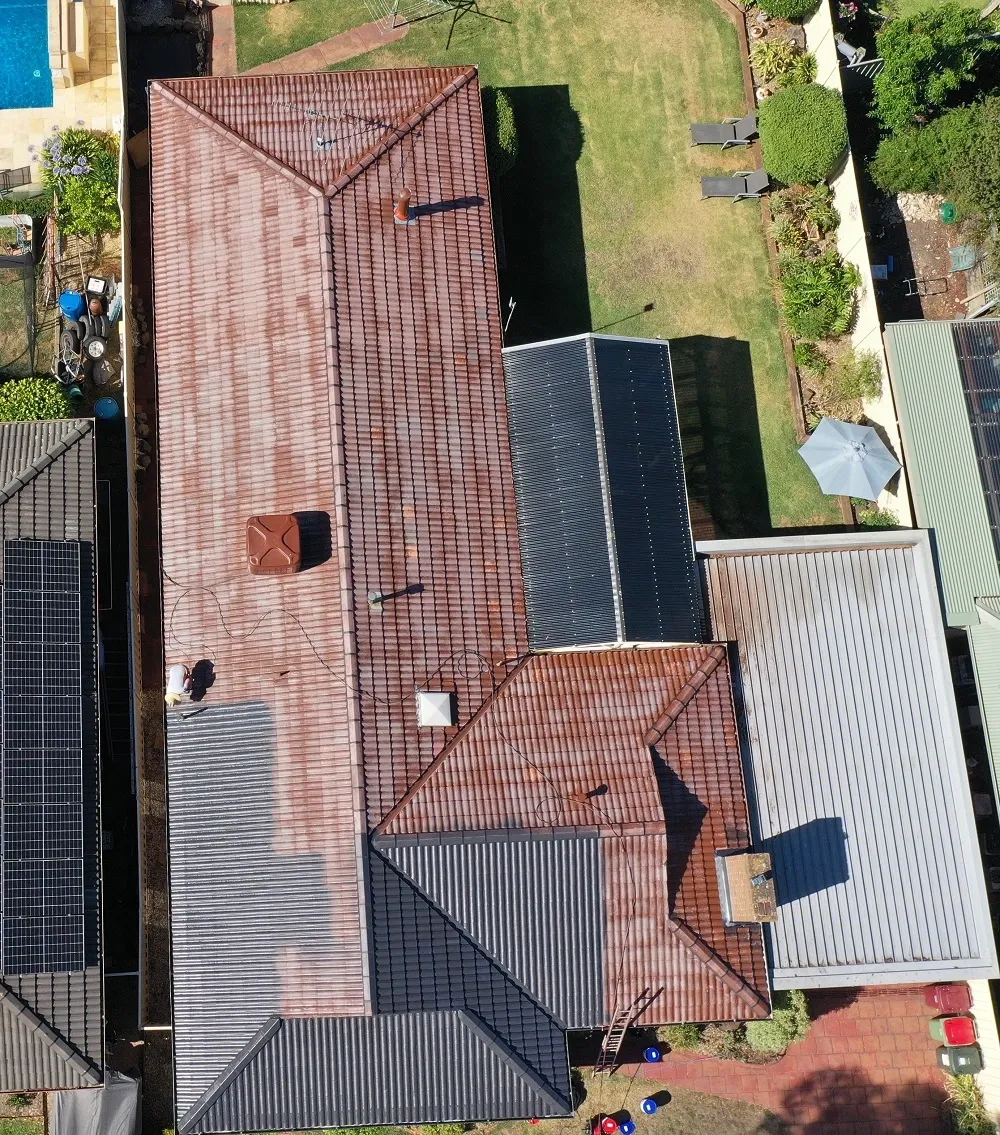 Drone view of a terracotta tiled roof part-way through a charcoal membrane coating